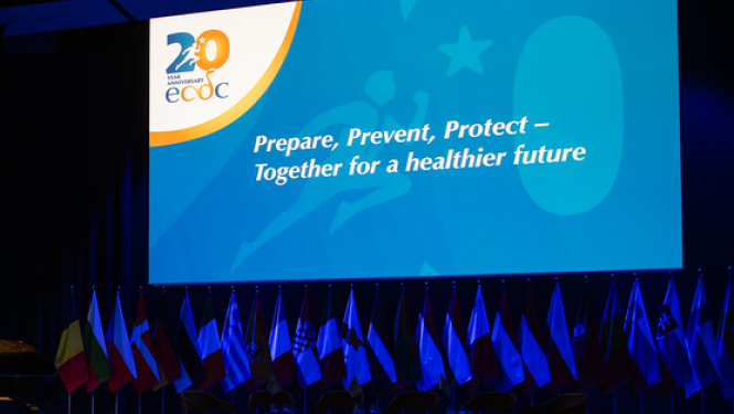 Eiropas slimību profilakses un kontroles centra 20 gadu svinību oficiālais foto. Svinību zāle ar plakātu. Uzraksts uz plakāta: "Gatavoties, novērsts, pasargāt".
