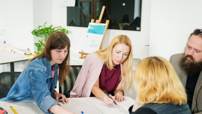 Četri cilvēki sēž ap galdu un pilda uzdevumus