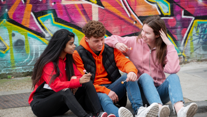 Trīs jaunieši sēž uz trotuāra