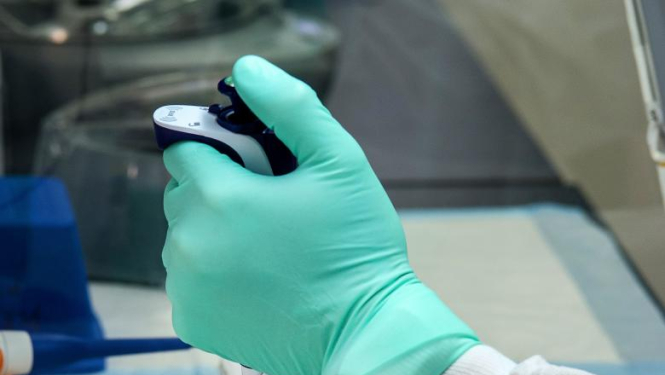 Laboratorijas galds uz kura medicīnas darbinieks ar zaļiem medicīnas cimdiem veic analīzes ar labaratorijas ierīcēm