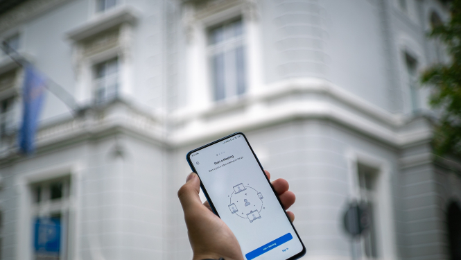 Mājas fonā roka tur paceltu tālruni