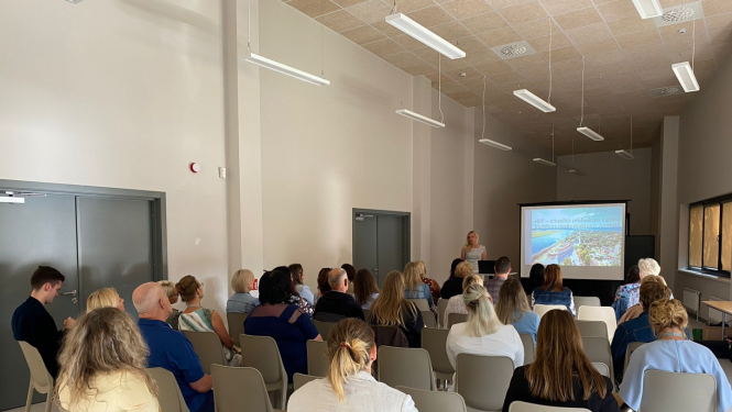 Cilvēki sēž krēslos un vēro prezentāciju