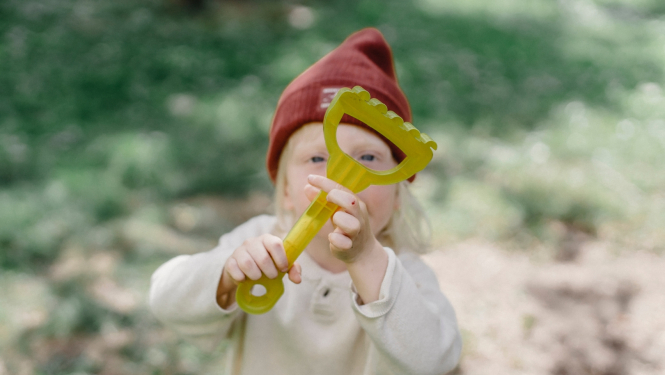 Vasarā bērns tur paceltu dārza grābekli