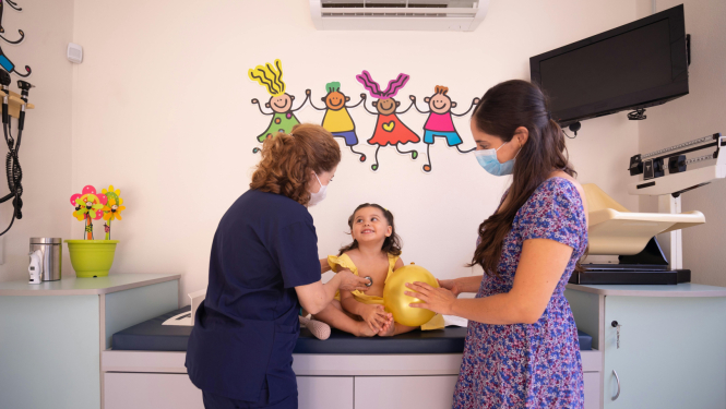 mamma violetā kleitā pie ārsta uz apksti ar mazu meitenīti