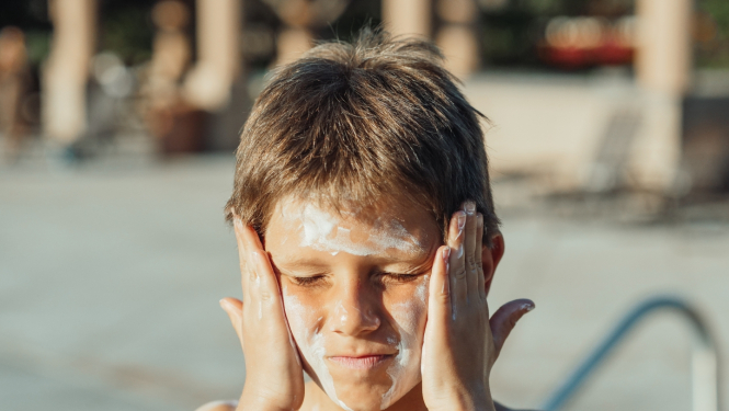 Zēns pie baseina smērē saules aizsargkrēmu uz sejas