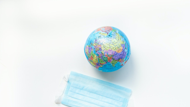 Uz balta fona globuss un medicīnas maska