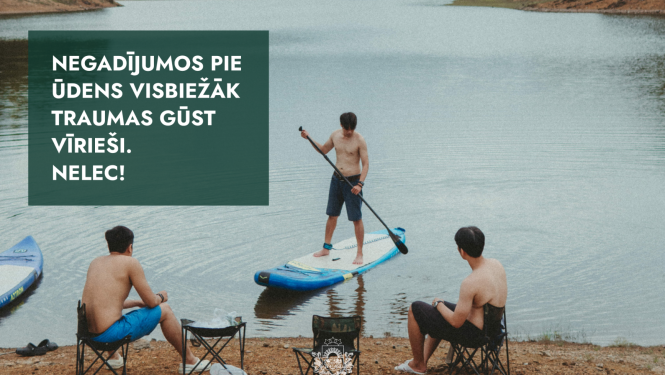 cilvēki atpūšas pie ūdens, divi sēž krastā, viens uz supa ūdenī