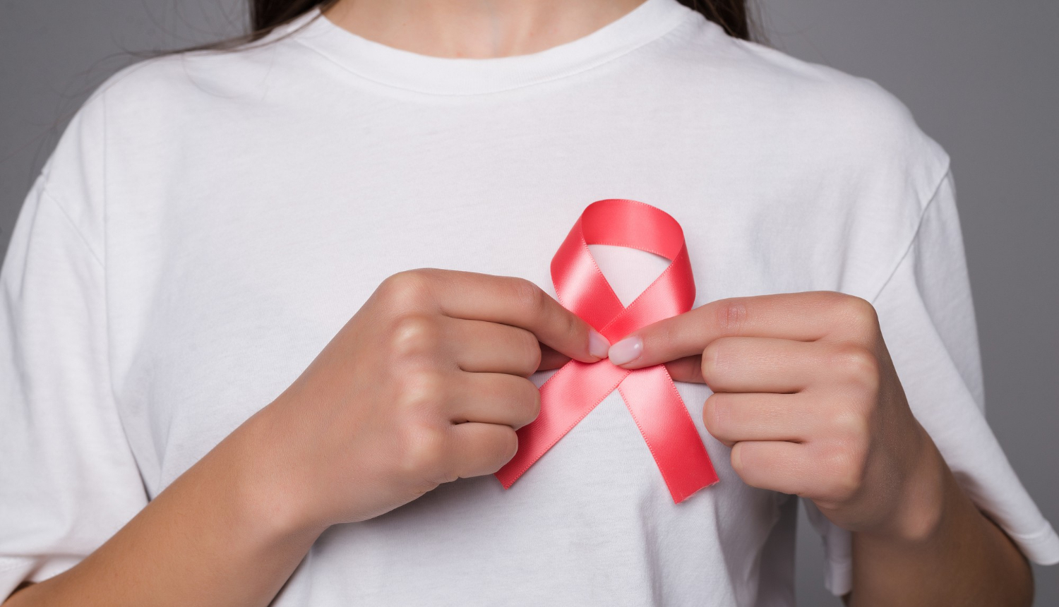 Sieviete baltā T-kreklā pielikusi pie krūts rozā lentīti