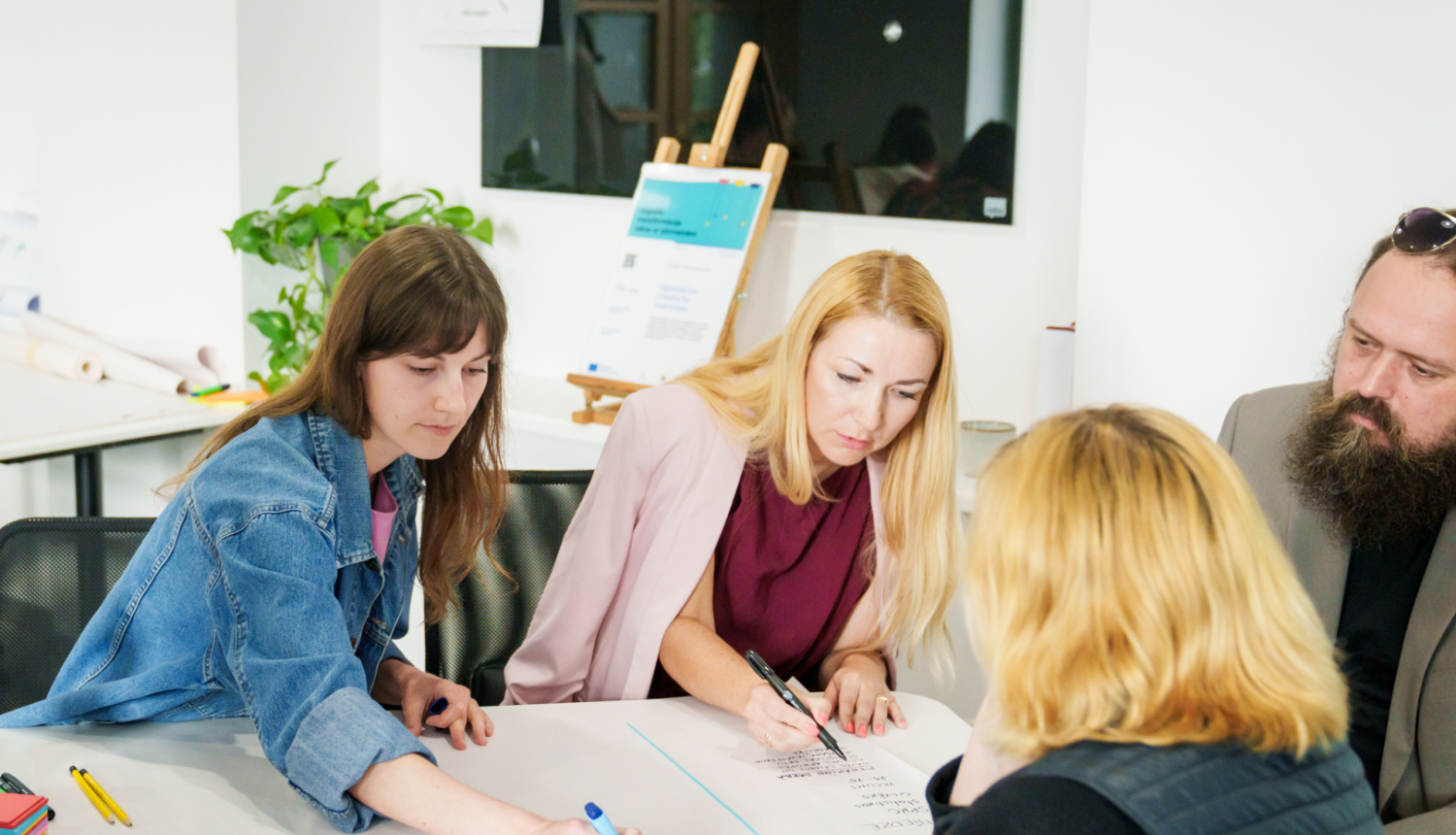 Četri cilvēki sēž ap galdu un pilda uzdevumus