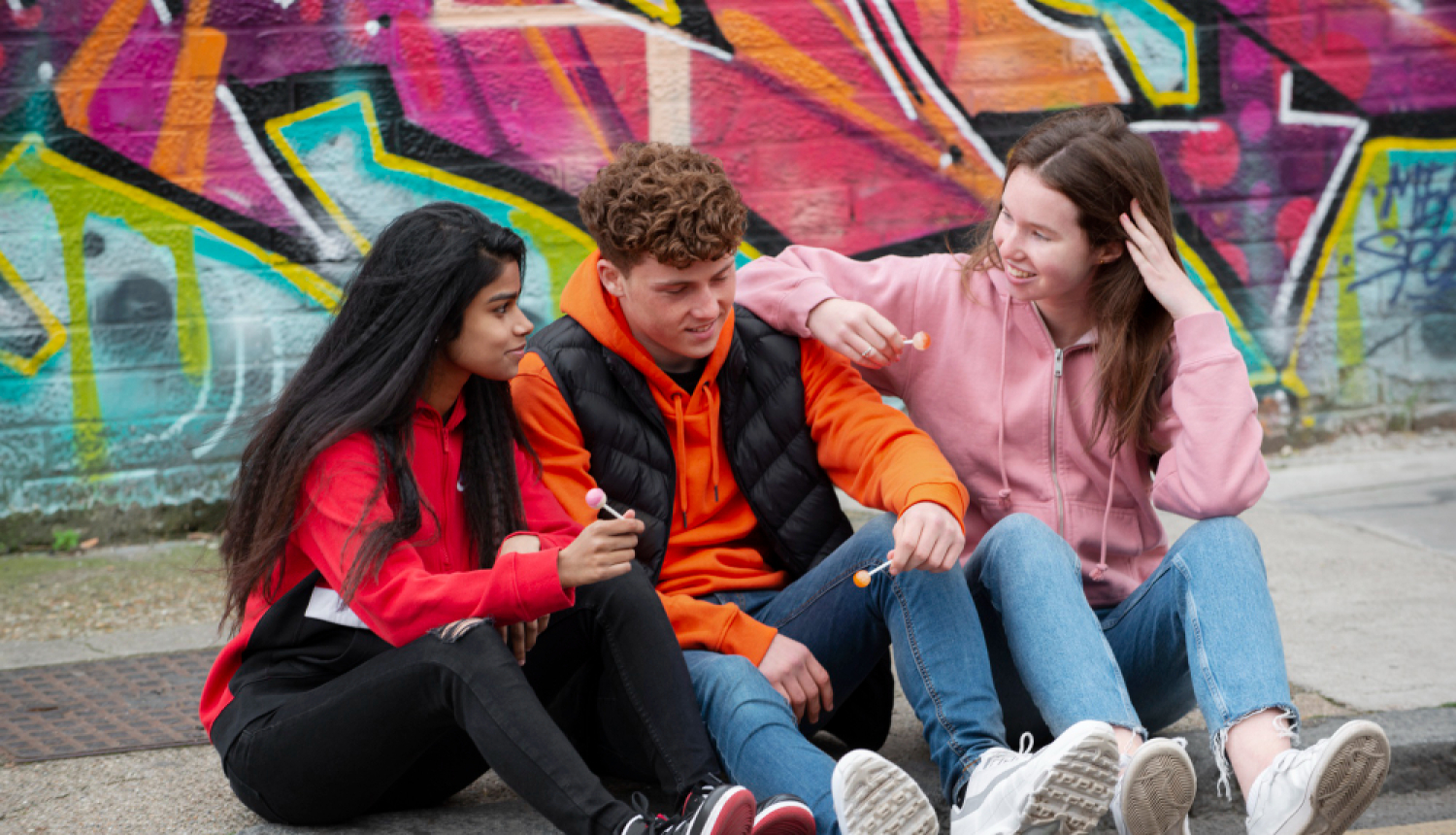 Trīs jaunieši sēž uz trotuāra