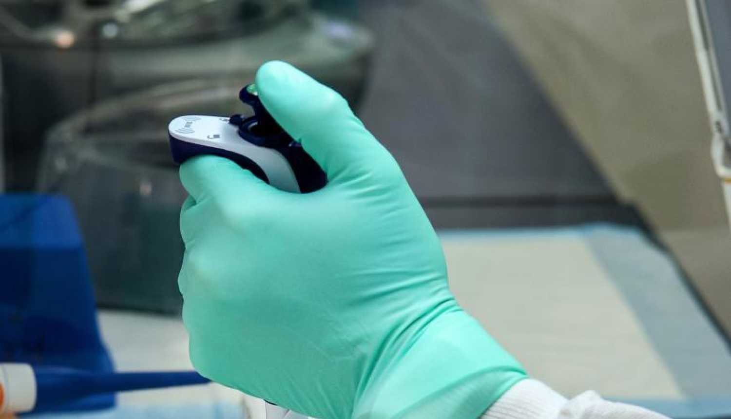 Laboratorijas galds uz kura medicīnas darbinieks ar zaļiem medicīnas cimdiem veic analīzes ar labaratorijas ierīcēm