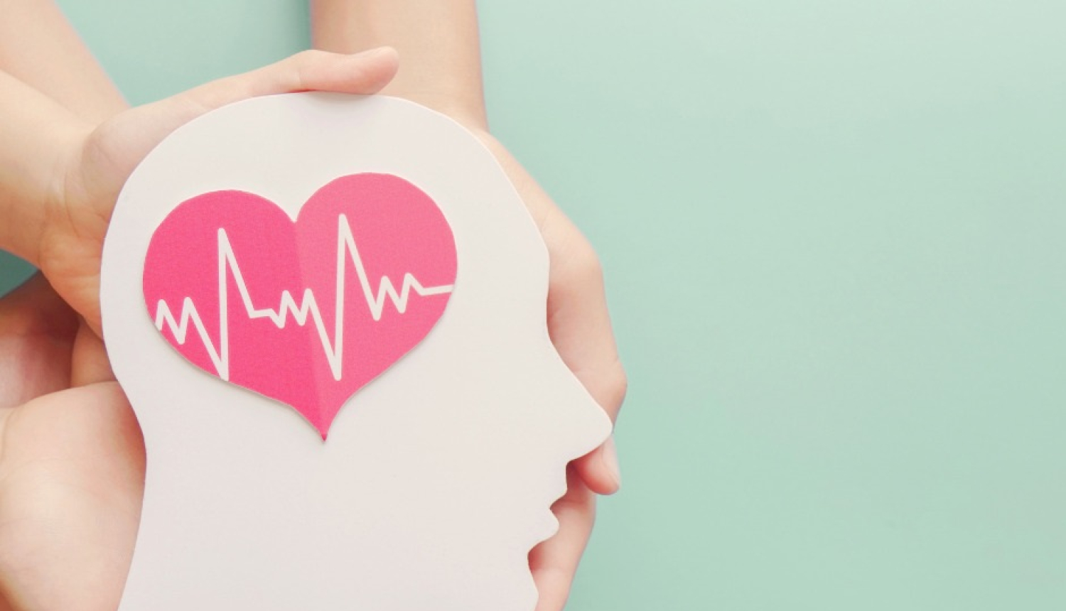 uz gaisī zaļa fona cilvēku rokas tur galvu,kuraiuzzīmēta sirds ar kardeogrammas rakstu