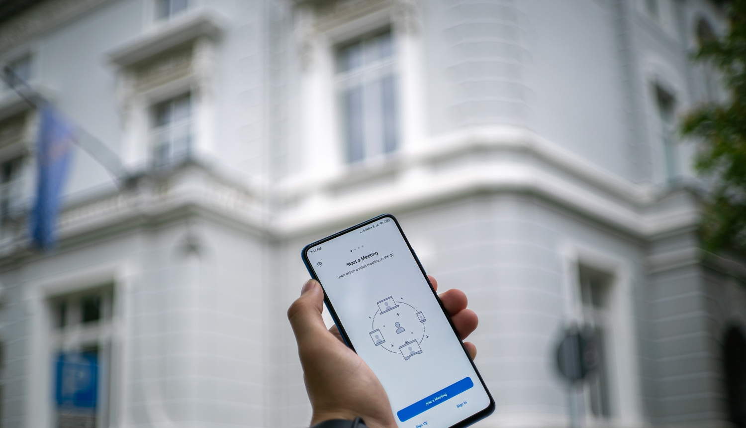 Mājas fonā roka tur paceltu tālruni