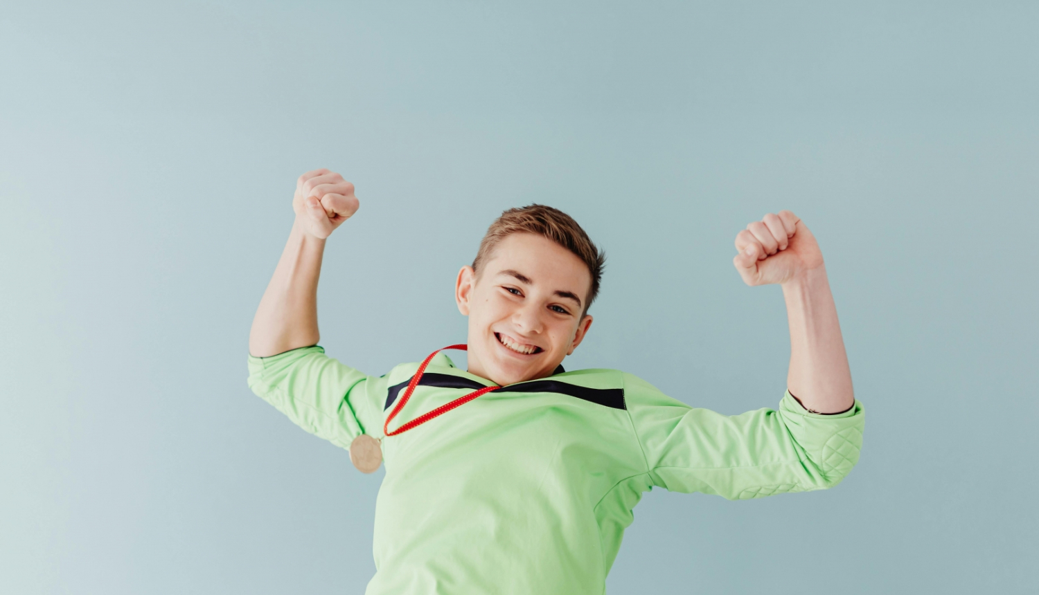 Uz pelēka fona priecīgs pusaudzis zaļā kreklā