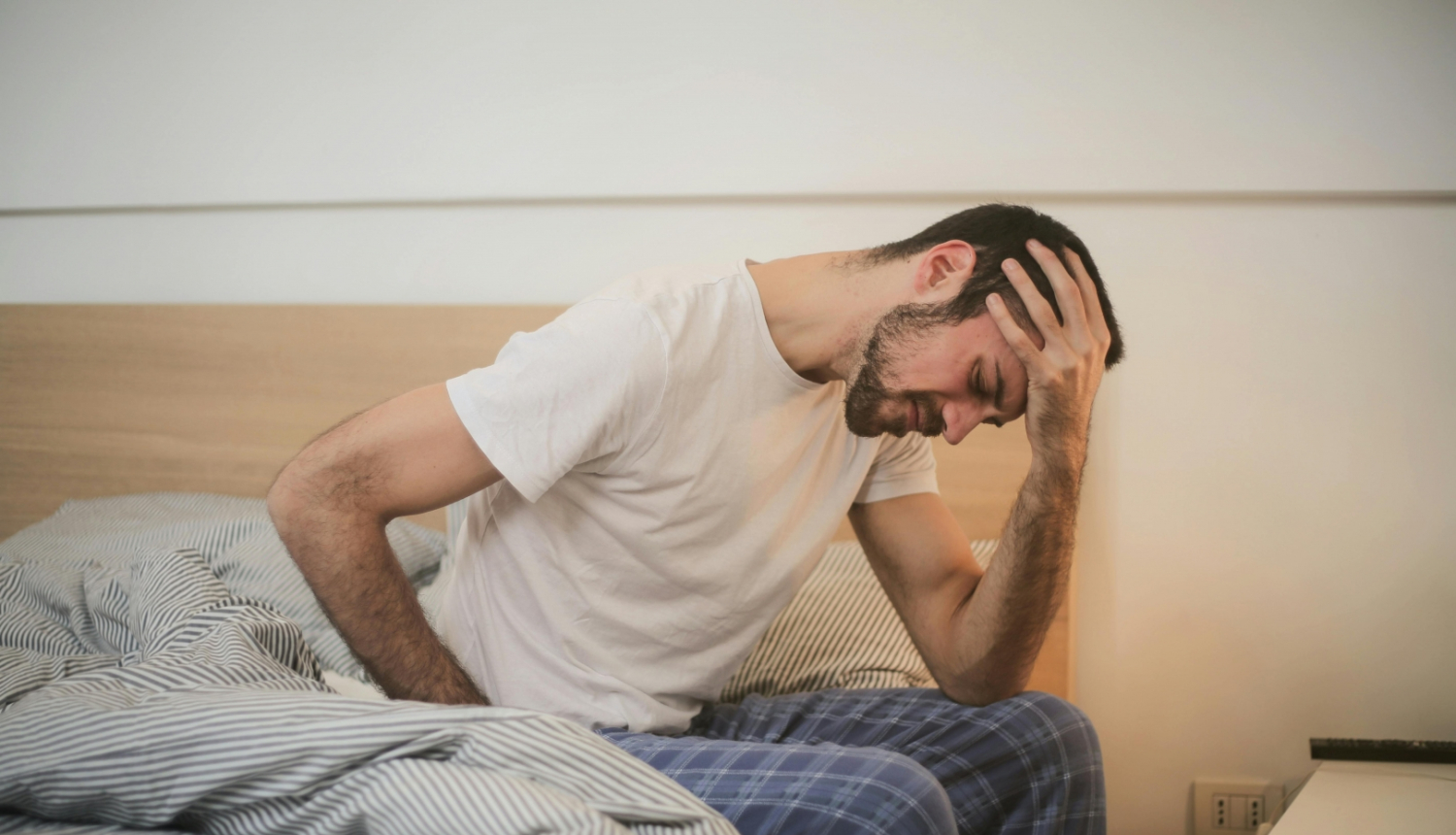 Slims vīrietis sēž uz gultas malas